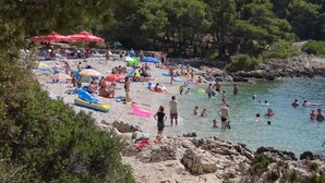 Una playa con gente nadando y tomando el sol, rodeada de árboles y terreno rocoso.