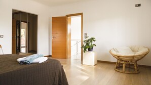 Un dormitorio con una cama, una silla, una planta en maceta y una puerta que da a otra habitación.