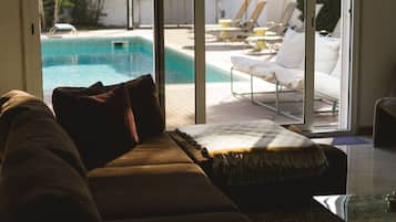 Ett vardagsrum med en soffa, utsikt över en pool och solstolar utomhus.