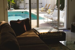 Ett vardagsrum med en soffa, utsikt över en pool och solstolar utomhus.
