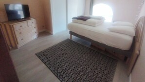 Ein Schlafzimmer mit einem Bett, einem Fernseher auf einer Kommode, einem gemusterten Teppich und einem Fenster mit Vorhängen.