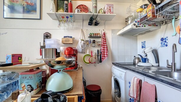 Eine kompakte Küche mit Waschmaschine, Kaffeemaschine sowie verschiedenen Küchenutensilien und Geräten.