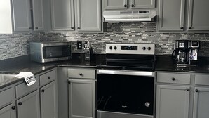 A modern kitchen with grey cabinets, a stainless steel range, a microwave, and a coffee maker. - Spacious DC Townhome (Washington)