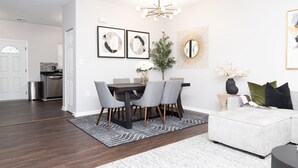 A modern living room with a dining area, featuring a dark wood dining table, grey upholstered chairs, a white sofa, and a patterned rug. - Spacious DC Townhome (Washington)