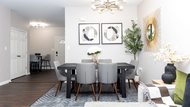 A dining area with a dark wood table, grey chairs, and a chandelier. There are two framed abstract artworks on the wall, a mirror with a sunburst design, and a potted plant. - Spacious DC Townhome (Washington)