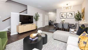 A modern living room with a flat-screen TV, a dining area with a table and chairs, and a staircase. - Spacious DC Townhome (Washington)