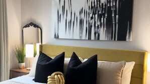 A modern bedroom with a bed, a headboard, a bedside table, a lamp, a mirror, and a painting on the wall. - Spacious DC Townhome (Washington)