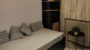 Een kleine, knusse kamer met een bed, een radiator en een tafeltje met een plant.