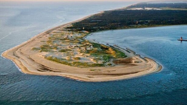 Eine Vogelperspektive einer Küsteninsel mit einem Leuchtturm, umgeben von Wasser und Vegetation.