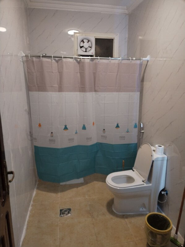 Un baño con inodoro, cortina de ducha, ventilador de techo y cubo de basura.
