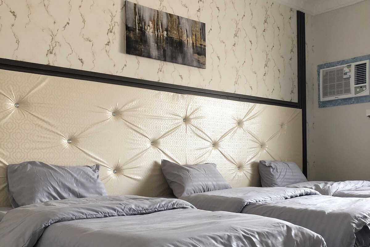 A hotel room with two beds, a marble-patterned wall, a ceiling light fixture, and a painting.