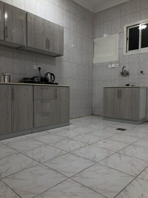 A kitchen with grey cabinets, a tiled floor, and a window with a white blind. - Al Ghazali Suites (Madinah)