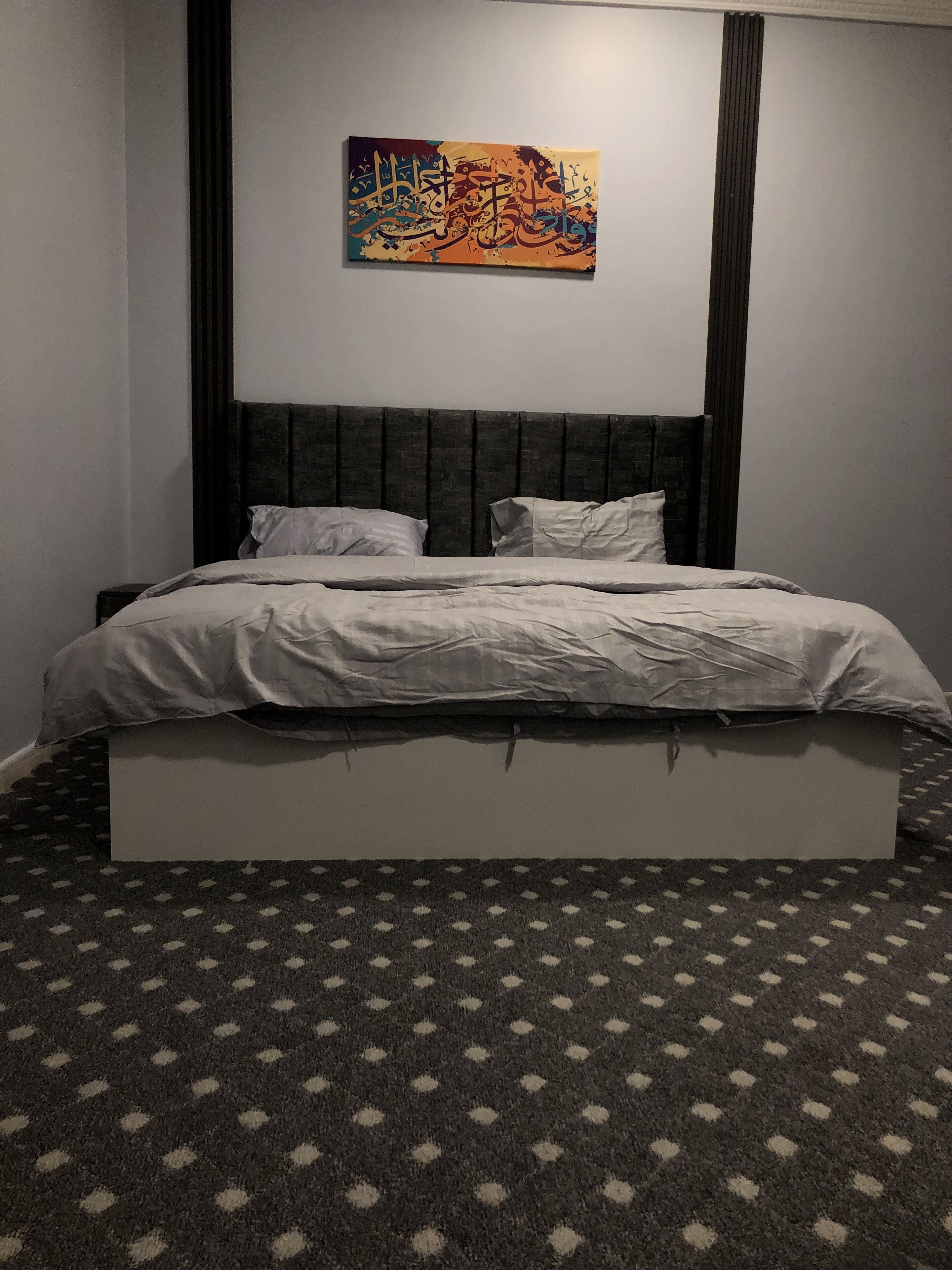 A bed with a white mattress and pillows, a dark headboard, and a patterned carpet.
