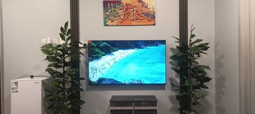 A television mounted on a wall displaying a beach scene, flanked by two potted plants.
