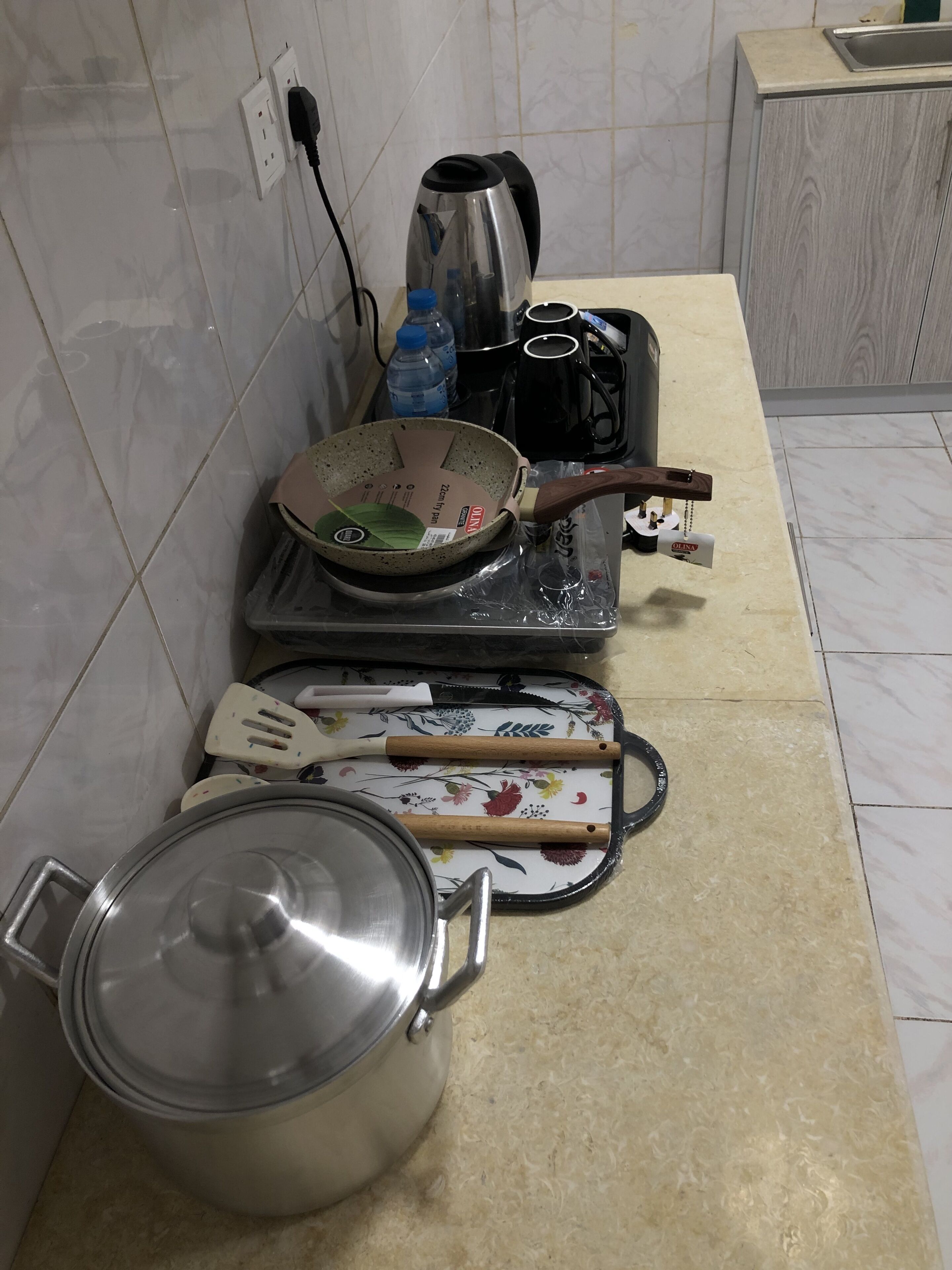 Una cocina con estufa, hervidor, sartén, espátula y olla.