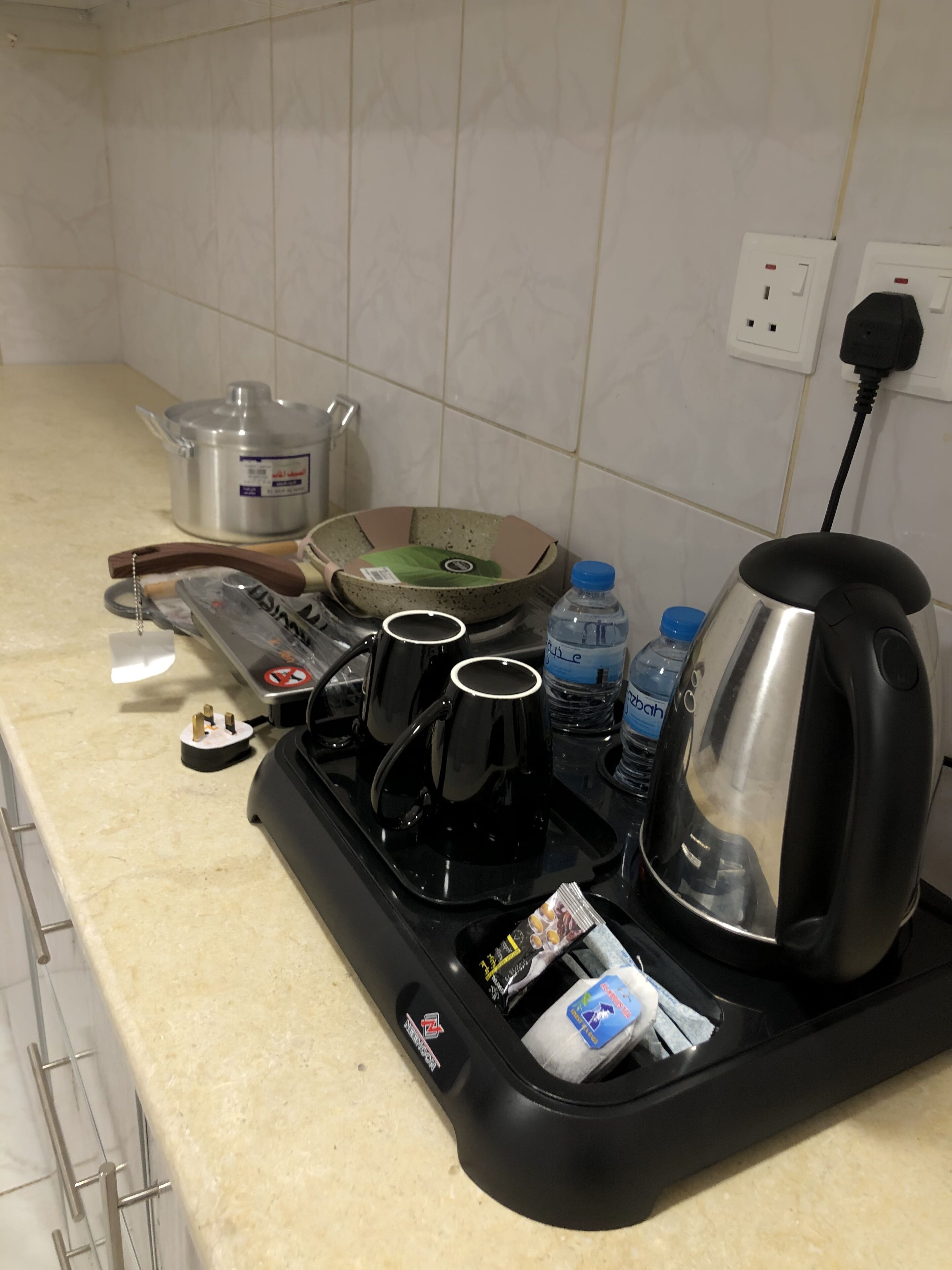 A kitchen counter with a coffee maker, mugs, a kettle, a pot, and a bottle of water.