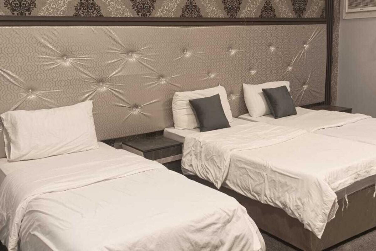A hotel room with two single beds, a large padded headboard, and a small bedside table.