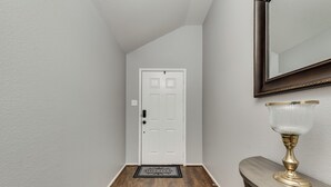 A hallway with a white door, a doormat, and a lamp on a console table.
