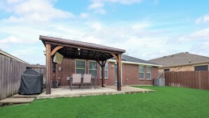 A backyard with a covered patio, a grill, and a well-maintained lawn.