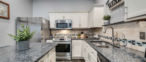 A modern kitchen with stainless steel appliances, white cabinetry, granite countertops, and a tiled backsplash.