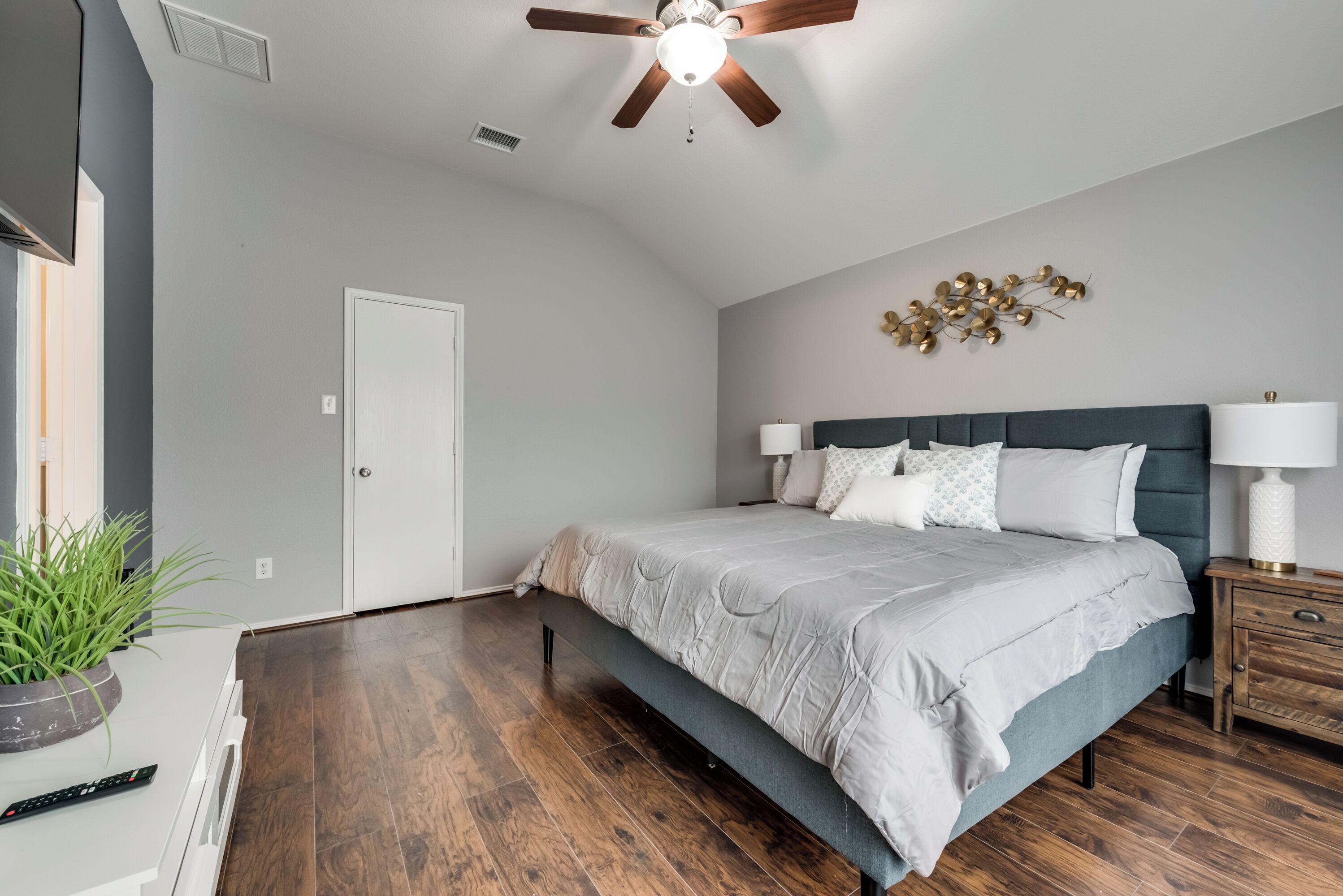 A bedroom with a bed, bedside tables, a ceiling fan, and a wall-mounted decorative piece.