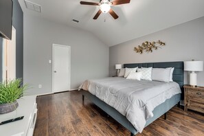 Quarto com cama, mesas de cabeceira, ventoinha no teto e um objeto decorativo na parede.