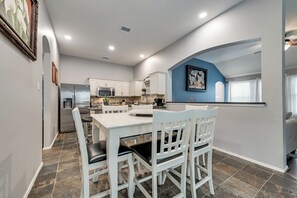Una cocina moderna con armarios blancos, una isla central y un comedor con sillas blancas.