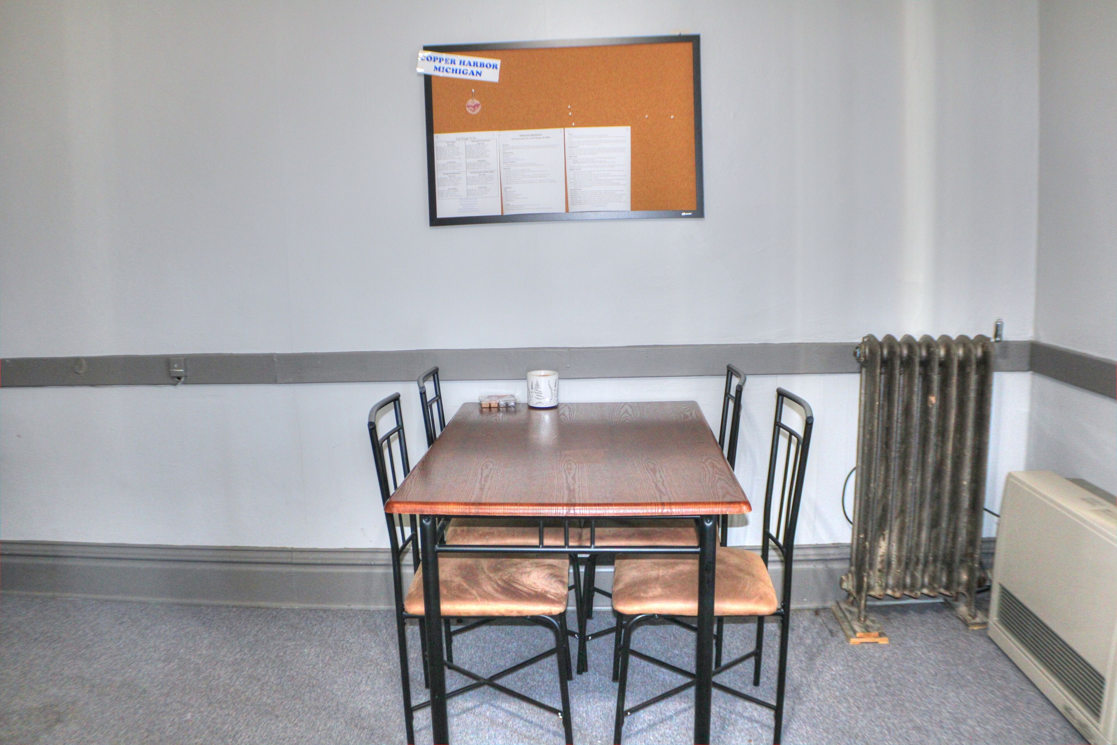 Une pièce comprenant un tableau d’affichage, une table, quatre chaises et un radiateur.