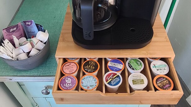 Une machine à café Keurig posée sur une table en bois, avec un tiroir contenant différents types de dosettes de café.