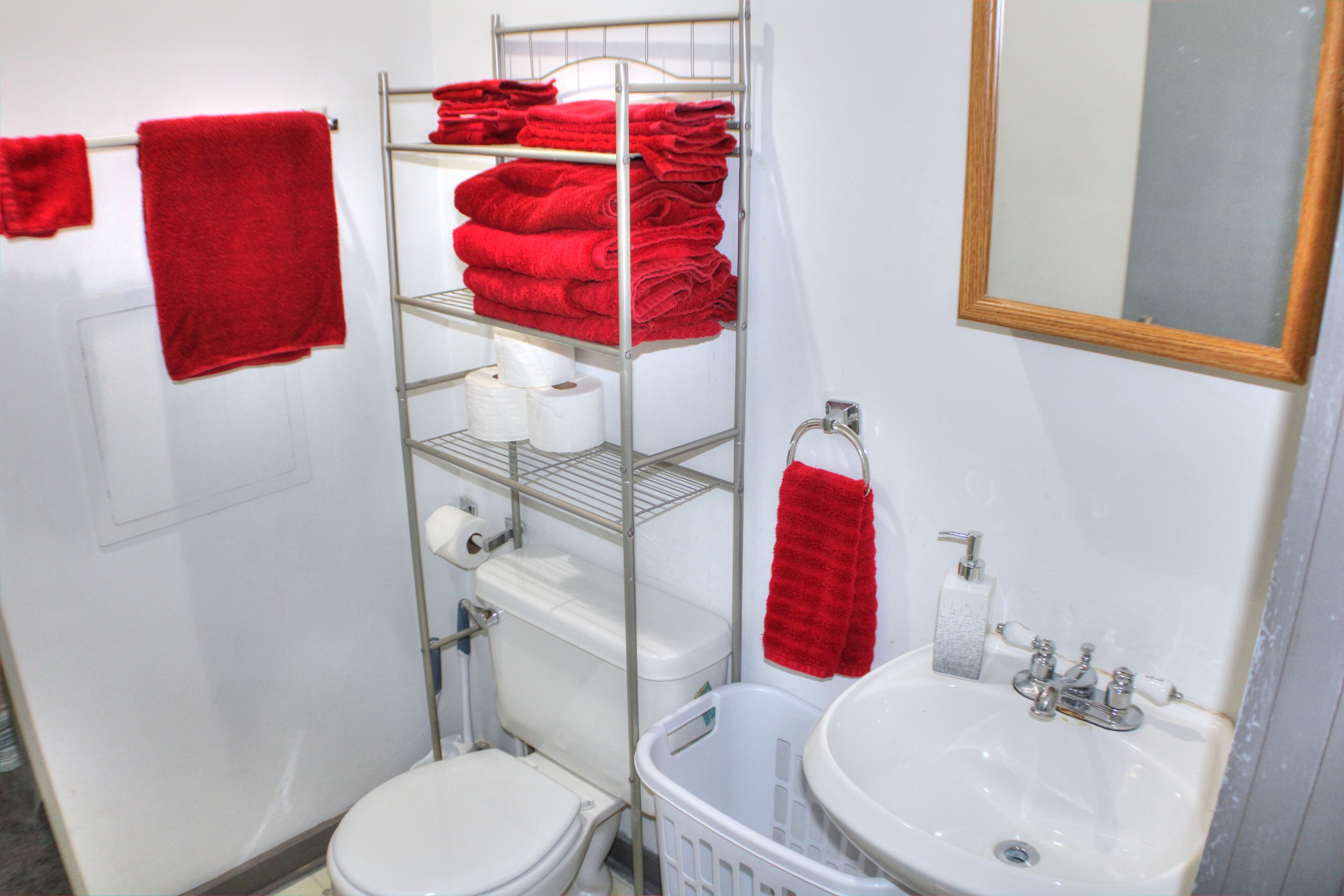 Een badkamer met toilet, wastafel en planken met rode handdoeken.