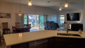 A modern kitchen with a central island, a dining area with chairs, a sofa, and a TV mounted on the wall.