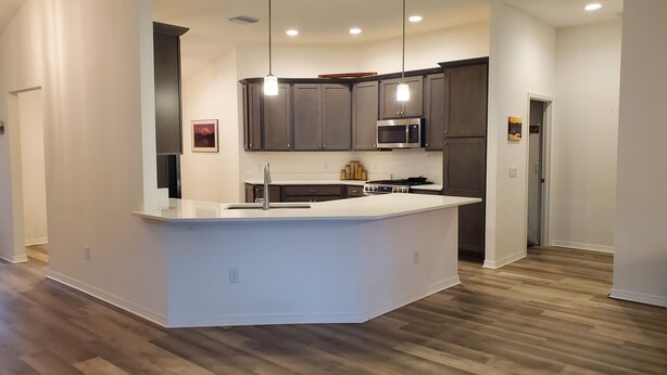 A modern kitchen with a central island, dark cabinets, stainless steel appliances, and pendant lighting.