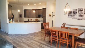 A modern kitchen with dark cabinets, a central island, and a dining area with wooden chairs and a table.