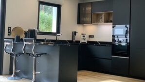 A modern kitchen with a central island, bar stools, and built-in appliances. - Maison Avec Piscine. Animaux de Compagnie Acceptés (La Tremblade)