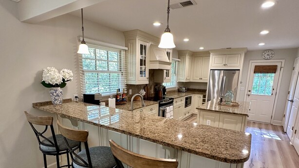 A spacious kitchen with a large island, bar stools, granite countertops, and white cabinetry. - Private Sea Pines Home w Large Deck. Great for couples! (Hilton Head Island)
