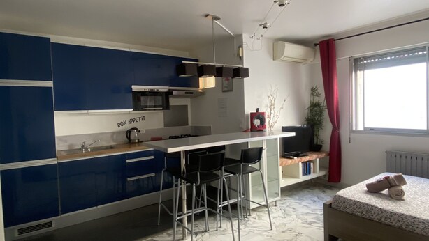 Eine kleine Küche mit blauen Schränken, einer weißen Arbeitsplatte und einer Bar mit Barhocker.