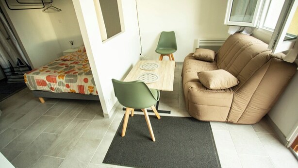 A compact living space with a sofa, a small table, two chairs, a bed with a colorful bedspread, and a window with a view. - Log'Appart, calm, comfort, wifi AUDENGE (Audenge)
