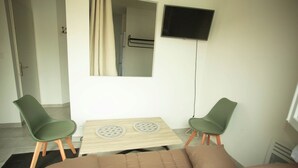 A small, well-lit room with a bed, two green chairs, a small table with a decorative item, a flat-screen TV mounted on the wall, and a window with curtains. - Log'Appart, calm, comfort, wifi AUDENGE (Audenge)