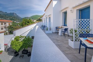 A balcony with outdoor seating, a table with food, and a view of mountains. - Villa Azzurra (Vico Equense)