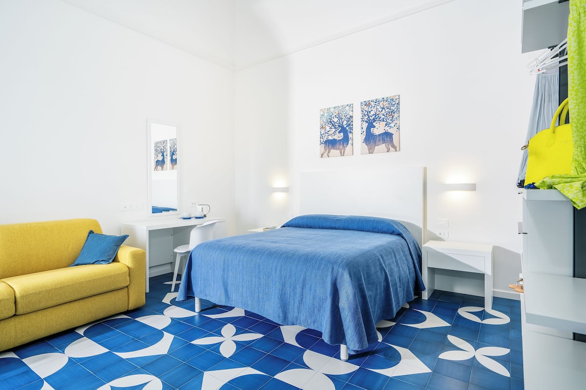A hotel room with a bed, a yellow sofa, a desk, and a chair.