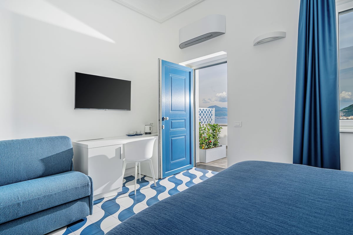 A modern hotel room with a large bed, a desk, a chair, and a TV.