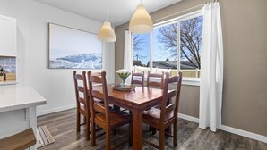 A dining area with a wooden table and chairs, a vase with flowers, and a window with a view of a snowy landscape. - Stationary bike|1600ft²|Backyard|Parking|300Mbps (Nampa)