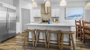 A modern kitchen with a central island, stainless steel appliances, wooden stools, and pendant lighting. - Stationary bike|1600ft²|Backyard|Parking|300Mbps (Nampa)