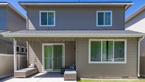 A two-story house with a covered patio area, a sliding glass door, and a small outdoor seating area with cushions. - Stationary bike|1600ft²|Backyard|Parking|300Mbps (Nampa)