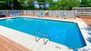 A rectangular swimming pool with a wooden deck, surrounded by a wooden fence and trees.