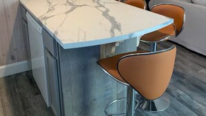 A kitchen with a marble countertop, two bar stools, and a built-in dishwasher.