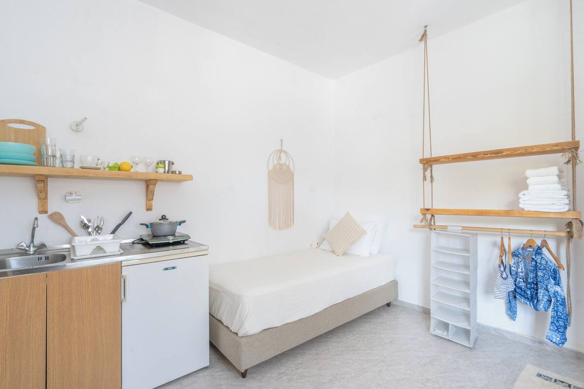 Ein gemütlicher Raum mit Küchenzeile, einem Bett, einer Wanddekoration aus Makramee und einem Kleiderständer.