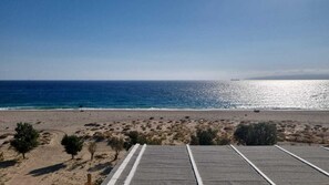 A beach with a paved area in the foreground, a clear view of the ocean, and a distant ship on the horizon. - Despoina Rooms Potami (Karystos)