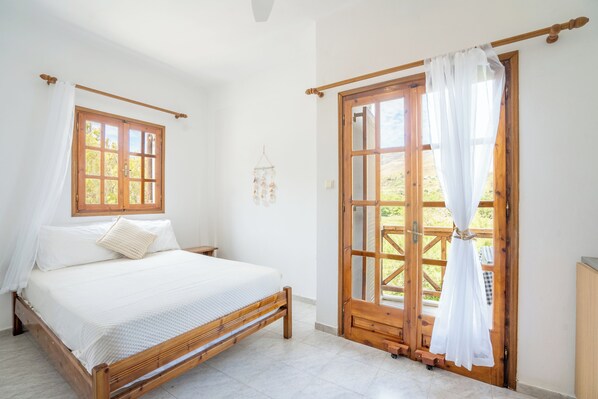 Een slaapkamer met een houten bed, witte beddengoed, een houten deur met uitzicht en een klein nachtkastje.