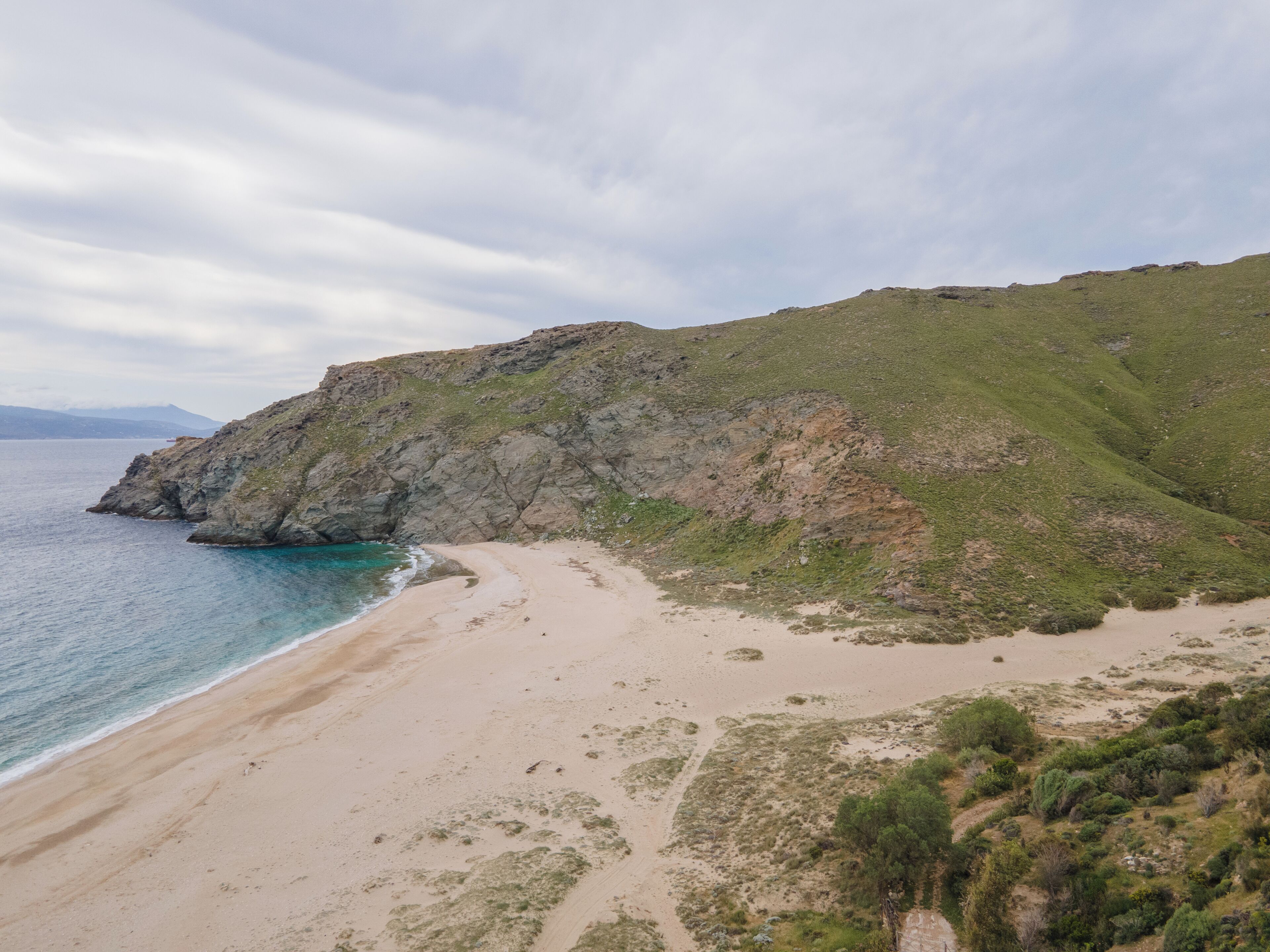 Un paisaje costero con una playa de arena, acantilados rocosos y vegetación escasa.